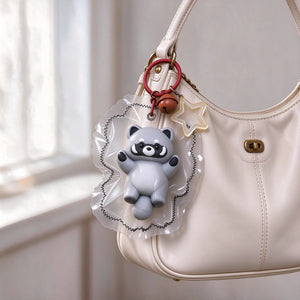 Raccoon-shaped squishy charm displayed hanging from a handbag.