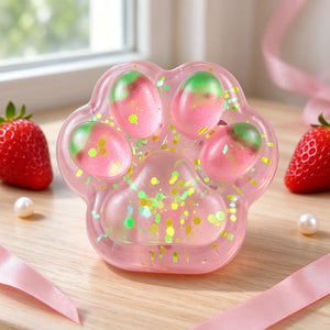 Translucent pink cat paw squishy with colorful glitter and rounded toe pads on a pink background.