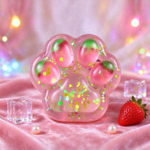 Pink cat paw squishy with glittery toe pads displayed beside strawberries.