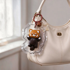 Brown raccoon-shaped squishy charm hanging from a handbag.