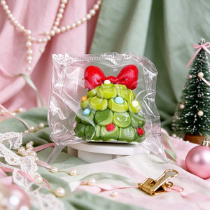 Close-up of a green Christmas tree-shaped squishy charm with a red bow.