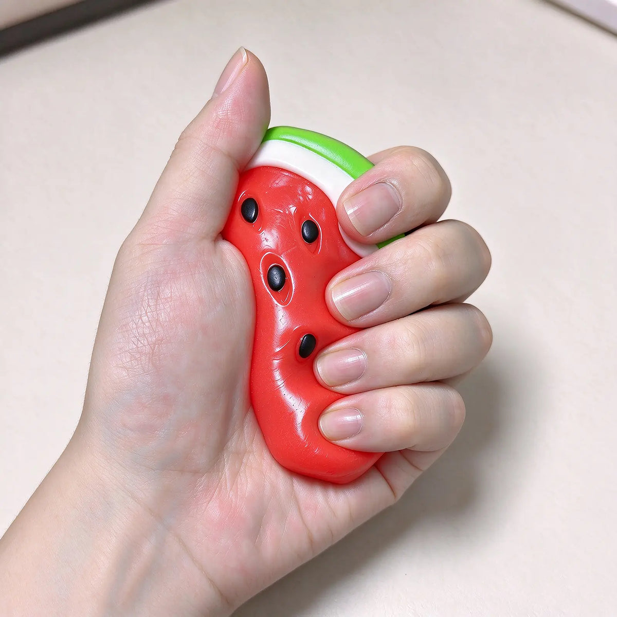 A hand holding a red watermelon-slice squishy to show its size.