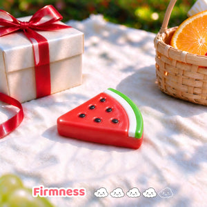 Watermelon-slice squishy displayed on a picnic table beside a gift basket.
